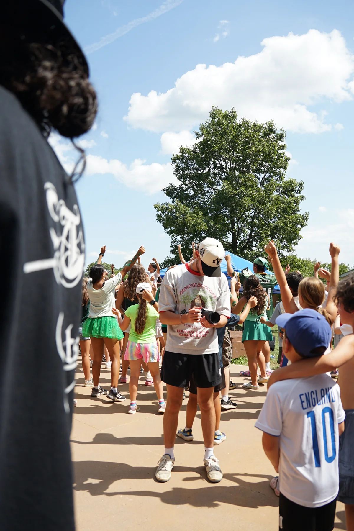 Zachary Black with his camera in the middle of a crowd of cheering kids on a sunny day
